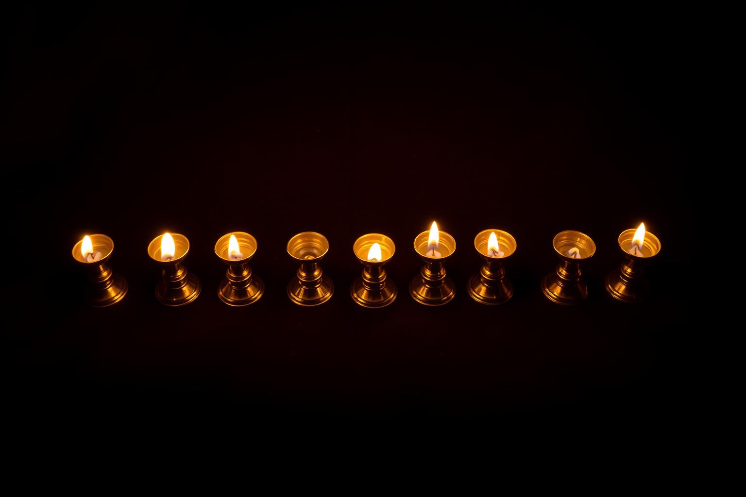 Ten brass oil lamps in a row, five glowing brightly and five dim